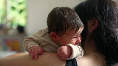 Ebeveynlerinin omzunda yeni doğmuş bir bebek, merakla bakıyor. Samimi an sevgi ve sıcaklıkla doludur. Bebeğin ebeveyninin kollarında hissettiği güven ve bağı yakalar.
