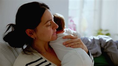 Anne yeni doğmuş bebeğini güneş ışığıyla kucaklıyor, sıcak bir ev ortamında samimi ve huzurlu bir bağ kurma anını gösteriyor.