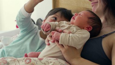 Anne, büyük kardeş bakarken bebeğini kucaklar ve şefkatli bir aile anı yaratır. Büyük çocuklar bebeğe bakıyorlar. Bu samimi sahnede merak ve kardeşlik bağı oluşuyor. 