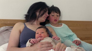 Anne yeni doğmuş ve büyük çocuğuyla bir not okuyor, yatakta samimi aile anlarını paylaşıyor, samimi ve sevgi dolu atmosfer, yakın çekim ve birliktelik, hassas ve huzurlu sahne