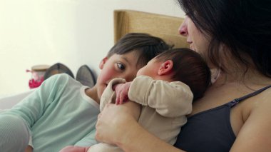 Anne, büyük kardeş bakarken bebeğini kucaklar ve şefkatli bir aile anı yaratır. Büyük çocuklar bebeğe bakıyorlar. Bu samimi sahnede merak ve kardeşlik bağı oluşuyor. 