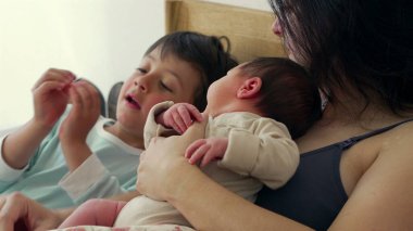 Anne, büyük kardeş bakarken bebeğini kucaklar ve şefkatli bir aile anı yaratır. Büyük çocuklar bebeğe bakıyorlar. Bu samimi sahnede merak ve kardeşlik bağı oluşuyor. 