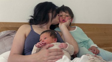 Anne yeni doğmuş ve büyük çocuğuyla bir not okuyor, yatakta samimi aile anlarını paylaşıyor, samimi ve sevgi dolu atmosfer, yakın çekim ve birliktelik, hassas ve huzurlu sahne