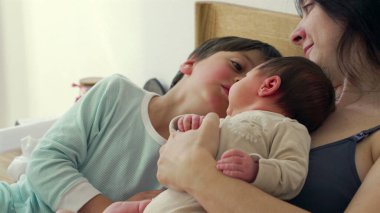 Anne, büyük kardeş bakarken bebeğini kucaklar ve şefkatli bir aile anı yaratır. Büyük çocuklar bebeğe bakıyorlar. Bu samimi sahnede merak ve kardeşlik bağı oluşuyor. 