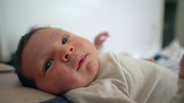 Mutlu yeni doğmuş bebek yatakta uzanıyor, sakin ve hoşnut yüz ifadesi, huzurlu ve rahat bir atmosfer, samimi aile anı, bebeklerin sakin tavırlarını, bağlanmalarını ve sevilmelerini vurgulayan detaylı yakın çekim 