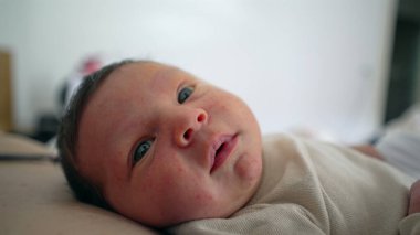 Mutlu yeni doğmuş bebek yatakta uzanıyor, sakin ve hoşnut yüz ifadesi, huzurlu ve rahat bir atmosfer, samimi aile anı, bebeklerin sakin tavırlarını, bağlanmalarını ve sevilmelerini vurgulayan detaylı yakın çekim 