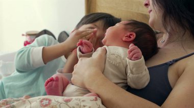 Anne, büyük kardeş bakarken bebeğini kucaklar ve şefkatli bir aile anı yaratır. Büyük çocuklar bebeğe bakıyorlar. Bu samimi sahnede merak ve kardeşlik bağı oluşuyor. 