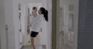 Anne koridorda karoları yansıtarak bebeği tutuyor, samimi otantik yaşam tarzı sahnesi, samimi aile anı, beslenme ve bağ kurma, sıcak ve doğal ışık