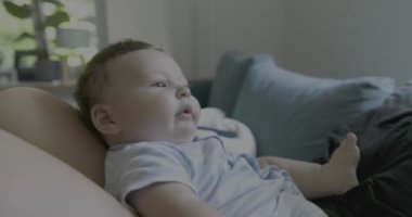 Anne oynarken bebeğini yüzüne yakın tutuyor, sıcak, aile dostu bir oturma odasında sevgi ve bağ anları, doğal ışıklandırma.