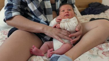 Yeni doğmuş bir bebek, beyaz tulum giymiş bir ebeveynin kucağında uzanıyor. Sıcak ve şefkatli bir ortamda yakın bir bağ ve rahatlık gösteriyor.