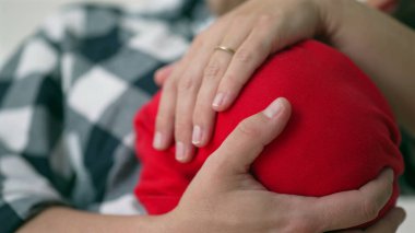 Bir annenin elinin yakın çekimi yeni doğan bebeğini nazikçe alt açıdan sarkıtıyor. Bağlarında şefkat ve özen