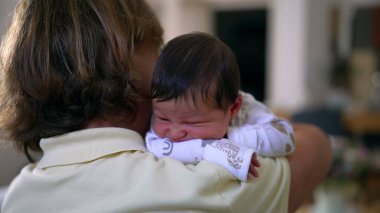 Yeni doğan bebek büyükannenin omzunda dinleniyor, bir anlık rahatlık ve güven yakalıyor, ailevi sevgi ve bağlılık gösteriyor.