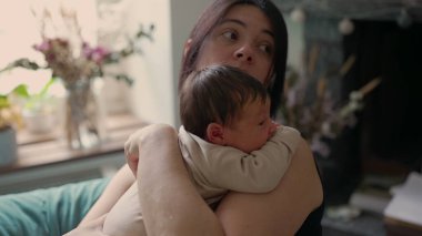 Anne yeni doğmuş bebeğini kucağında tutuyor ve etrafına sakin bir şekilde bakıyor. Sıcak, sıcak ortam, güvenlik ve sevgi hissini arttırır. Huzurlu ve samimi bir atmosfer yaratır.