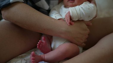 Yeni doğan bebek, beyaz tulum giymiş bir ebeveynin kucağında dinleniyor. Sıcak ve şefkatli bir ortamda yakın bir bağ ve şefkat gösteriyor.