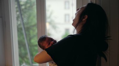Anne yeni doğmuş bebeğini bir pencerenin yanında tutuyor, esniyor, onu besliyor ve sıcak, samimi bir anda ebeveynliğin zorluklarını anlatıyor.