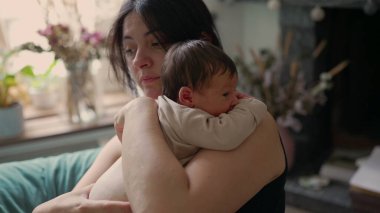 Anne yeni doğmuş bebeğini kucağında tutuyor ve etrafına sakin bir şekilde bakıyor. Sıcak, sıcak ortam, güvenlik ve sevgi hissini arttırır. Huzurlu ve samimi bir atmosfer yaratır.