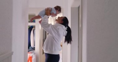 Anne sevinçle bebeğini havaya kaldırıyor, aydınlık bir koridorda sevgi dolu bir anı paylaşıyor. neşeli etkileşimler ve gülümsemeler anne ve çocuk arasındaki güçlü bağı ve mutluluğu gösterir.