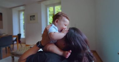 Anne ve bebek, parlak bir oturma odasında birlikte oynuyorlar. Neşeli anlar, kahkahalar ve doğal ışıklandırmayla bağ kuruyorlar.