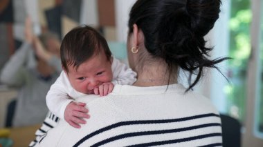Bir annenin bebeğini omzunda tutarken, bebek huzur içinde dinlenirken, yaşlı bir adamın arka planda biraz bulanıklaşması, sıcak ve besleyici bir sahne yaratıyor.