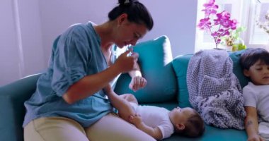 Anne çocuklarıyla kanepede vakit geçirir, diğer çocuk rahat ve sıcak bir evde dinlenirken bebeğiyle oynar.