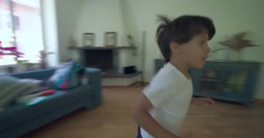 Çocuk koridorda parlak bir odaya koşuyor, hızlı bir sahneyi takip ediyor, çocuğun evdeki oturma alanına doğru hareketine odaklanıyor.
