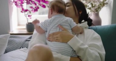 Anne bebeğini kucağına alır, onu nazikçe kucağına alır parlak ve rahat bir oturma odasında kanepede oturur, aile zamanının özünü yakalar.