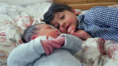 Ağabey, yeni doğan kardeşinin yanında yatıyor. Şefkatli ve düşünceli bir bakışla bakıyor. Huzurlu bir yuvada kardeşler arasındaki erken bağı ve sevgiyi gösteriyor.