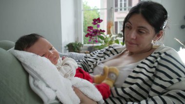 Anne ve yeni doğan anne, huzurlu bir yuva ortamında birbirine bağlanıyor. Anne düşünceli bir şekilde bebeğe bakıyor. Bitkiler ve doğal ışıkla çevrili.