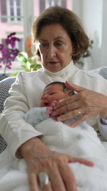 Büyükannesi yeni doğan torununa şefkatle dokunuyor. Huzurlu bir yuva ortamında derin bir bağ ve aşk anı yaşıyor.