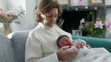 Büyükannem yeni doğan bebeği sıcak ve şefkatli bir şekilde kucaklıyor. Nesilleri huzurlu ve rahatlatıcı bir aile ortamında birbirine bağlayan derin bağları ve sevgiyi simgeliyor.
