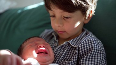 Ağlayan yeni doğmuş bir kardeşi olan genç bir çocuk, sıcak bir yuvadaki kardeşler arasındaki duygusal karmaşıklığı ve güçlü koruyucu bağı vurguluyor.