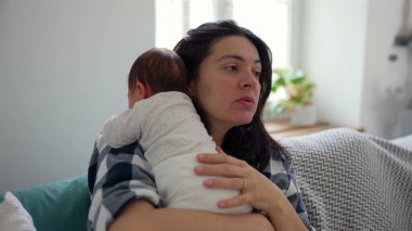 Yavrusunu kucağında tutan genç anne sıcak bir ev ortamında hassas ve koruyucu bir bağ kurma anını yakalıyor.