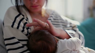 Anne sevecen bir şekilde yeni doğmuş bebeği güneş ışığıyla kucaklıyor, samimi ve huzurlu bir ev ortamında bağ kurma anını sergiliyor.