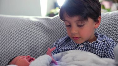 Ağabey, kucağında küçük kardeşiyle kucak kucağa yatarken ikisi de şefkatli bakışlar atıyor. Bu da güçlü bir kardeş bağının ve çocukluğunda aile sevgisinin sıcaklığını simgeliyor.