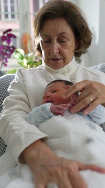 Büyükannesi yeni doğan torununa şefkatle dokunuyor. Huzurlu bir yuva ortamında derin bir bağ ve aşk anı yaşıyor.