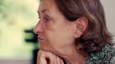 Düşünceli bir yüzü olan, çenesini elinin üzerine koyan yaşlı bir kadının yan profili. Doğal ışık yansıtıcı ve sakin tavrını geliştirir. Bilgeliğini ve sakinliğini ön plana çıkarır.