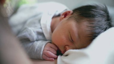 Yeni doğmuş bir bebeğin huzur içinde annesinin göğsünde uyuması huzurlu ve sevgi dolu bir ortamda paylaşılan yumuşak sıcaklığı, rahatlığı ve derin bağlantıyı vurguluyor.