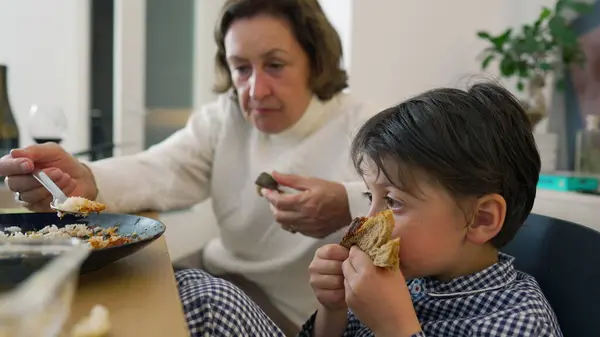 stock image Grandmother attentively feeding young boy at a dining table, highlighting familial love and care in a homey atmosphere. Bond between grandparent and grandchild