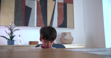 Genç Çocuk üzgün ve kızgın bir ifadeyle masada oturuyor, sakin bir ev ortamında hayal kırıklığı yaşıyor, aile ortamında duygular ve gerilim hissediyor.