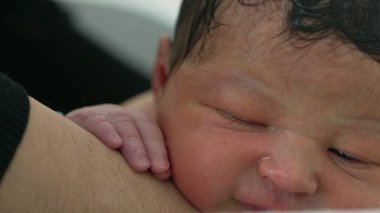 Yeni doğmuş bebek banyo yaparken sakin bir ifadeyle kolunda dinleniyor. Bu huzurlu anda bebeklerin narin özellikleri ve hassas bakımı sağlanıyor. 