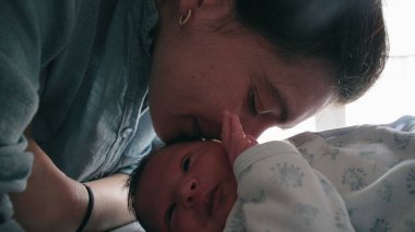 Anne, yeni doğmuş bebeğini sevgiyle kokluyor ve birlikte yatıp aralarındaki derin duygusal bağı gösteriyor. Erken yaşlardaki annelik bağının şefkati ve bakımı