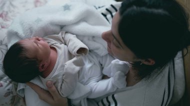 Anne, yeni doğmuş bebeğini kucağında kucağında kucaklar, bebek merakla etrafa bakar, samimi ve sıcak atmosfer, yumuşak ışık, besleyici bağ, yuva kurma