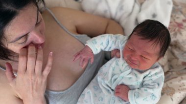 Anne, yeni doğmuş bebeğini nazikçe kucaklıyor. Bebek ağlıyor gibi görünüyor. Hayatının ilk günlerinde anne ve baba ile çocuk arasındaki bağın erken yaşta ortaya çıktığı duygusal bir an.