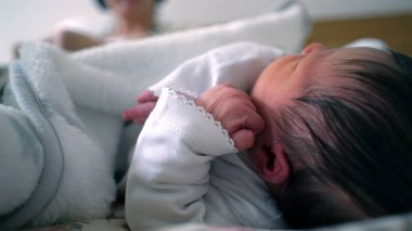 Yeni doğmuş bebek bir yatakta dinleniyor. Yüzlerine yakın bir elle yan yana uzanıyor. Sıcak ve güvenli bir ortamda, hassas bir uyku, rahatlık ve erken yaşam anı.