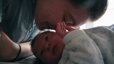 Anne, yeni doğmuş bebeğini sevgiyle kokluyor ve birlikte yatıp aralarındaki derin duygusal bağı gösteriyor. Erken yaşlardaki annelik bağının şefkati ve bakımı