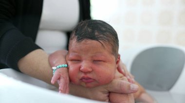 Newborn baby being lovingly cradled in a bath, with a hand gently resting on the baby's head for comfort and reassurance. baby's peaceful expression clipart