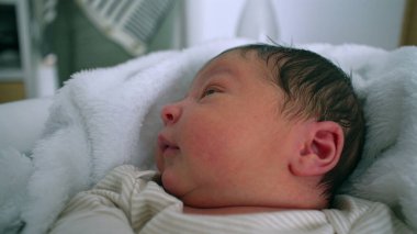 Yeni doğmuş bebek, yumuşak bir battaniyeye uzanmış meraklı gözlerle yukarı bakıyor. Bebeğin yüzündeki sakin ifade masumiyeti yansıtır, erken yaşlardaki huzuru yakalar.
