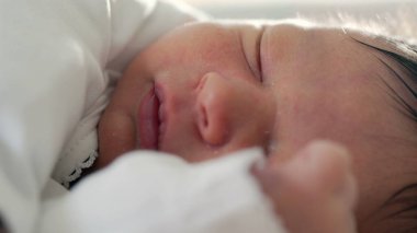 Yeni doğan bebek huzur içinde uyuyor. Yüzü ve eli yakın dinleniyor. Yumuşak ve güvenli bir ortamda, ilk yaşamın sıcaklığını, dinginliğini ve hassasiyetini yakalıyor.