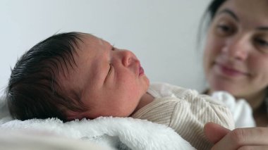 Yeni doğan bebek, annesinin kollarında dinleniyor, gözleri açık, sakin ifade, yakın çekim, annesine sevgiyle bakıyor, yakınlaşma ve şefkat anı, erken annelik.
