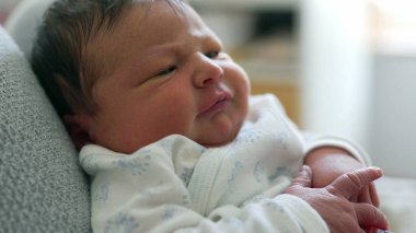 Gri dokulu bir yüzeyde dinlenen düşünceli bir yüzü olan yeni doğmuş bebek huzurlu ve sessiz bir ortamda rahatlık ve güvenlik hissi yayıyor.